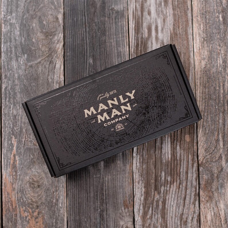 May include: A black box with a wood grain pattern and the text "quality gifts MANLY MAN COMPANY" in gold lettering.