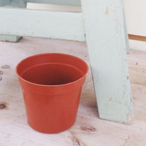 May include: A terracotta colored plastic plant pot with a smooth surface. The pot is empty and sitting on a wooden surface.