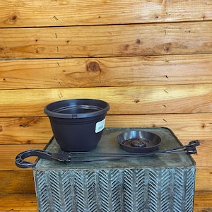 May include: A dark brown plastic plant pot with a matching saucer and hanging hardware. The pot has a rounded shape with a slightly flared rim. The saucer is circular with a central drainage hole. The hanging hardware is a dark brown color.