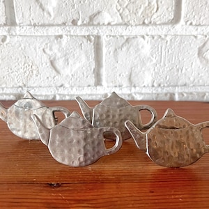 May include: Four silver teapot-shaped napkin rings with a hammered texture.