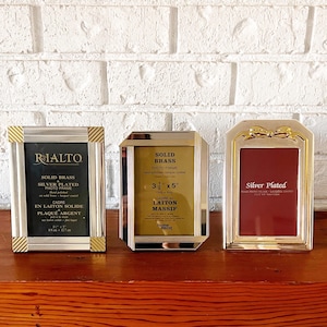 May include: Three silver and gold photo frames with varying designs. The frames are made of solid brass and silver plating. One frame has the text "RIALTO" and "SOLID BRASS". Another frame has the text "3 1/2" x 5"" and "SOLID BRASS". The third frame has a bow design.