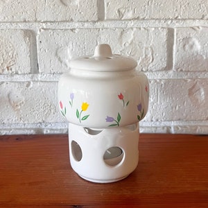 May include: White ceramic candle warmer with a floral design. The warmer has a removable top and a base with cutouts for candlelight to shine through.