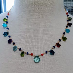 May include: A gold-tone chain necklace featuring a series of multi-colored, teardrop-shaped glass beads and small round beads in shades of red, blue, green, and turquoise, arranged symmetrically along the delicate metal link chain.