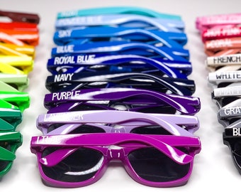 May include: A row of colorful sunglasses with different colored frames and lenses. Each pair has a different color name printed on the frame, such as "Orange", "Yellow", "Green", "Sky", "Blue", "Royal Blue", "Navy", "Purple", "French Vanilla", "Willie", "Gray", and "Black".