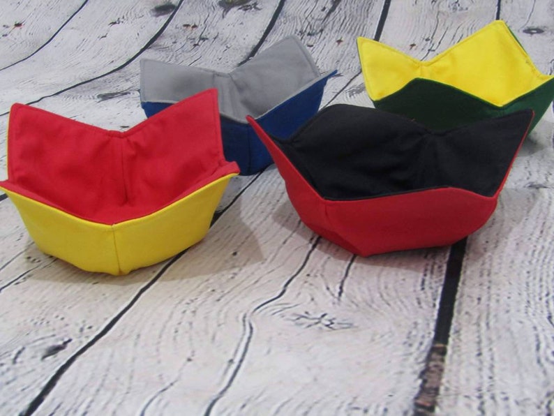 May include: Four fabric bowls in different colors. The bowls are folded into a bowl shape and are made of a soft, flexible fabric. The bowls are red, yellow, blue, and green.