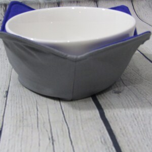 May include: A gray and blue fabric bowl cozy with a white ceramic bowl inside.