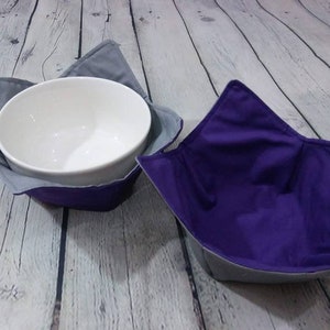 May include: Two fabric bowl cozies, one gray and one purple, with a white ceramic bowl inside the gray cozy.