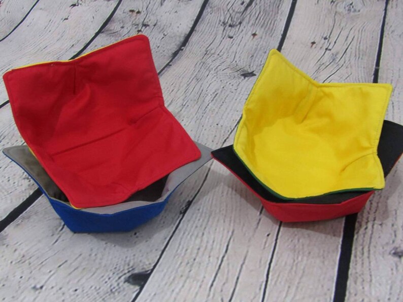 May include: Three fabric bowl cozies in red, yellow, and blue. The cozies are made of a soft, quilted fabric and are designed to protect bowls from heat and scratches.