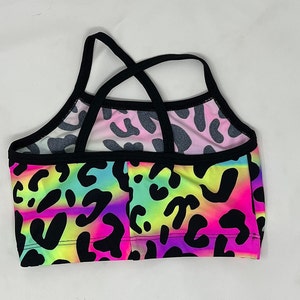 K&ouml;nnte beinhalten: Ein farbenfrohes Crop-Top mit einem lebendigen Leopardenmuster. Das Oberteil hat einen Regenbogen-Farbverlauf aus Neonfarben, darunter Pink, Gelb und Lila, mit schwarzen Leopardenflecken. Die Tr&auml;ger und der Besatz sind schwarz.