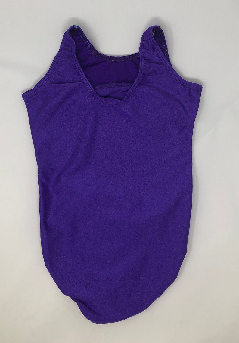 Puede incluir: Maillot de gimnasia morado liso con espalda escotada y tirantes. La ropa de gimnasia est&aacute; hecha de un material el&aacute;stico y est&aacute; dise&ntilde;ada para actividades deportivas. El maillot es de un tono morado vibrante.