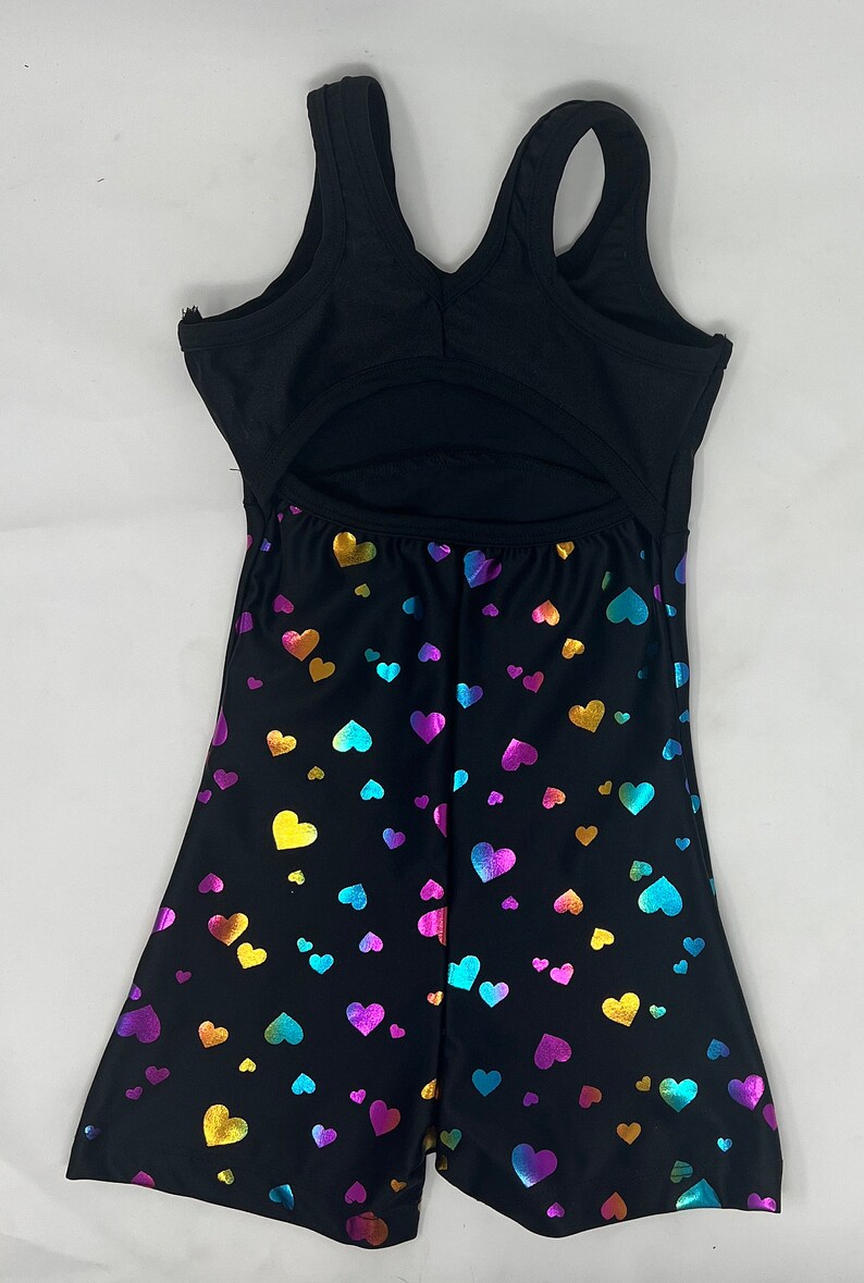 K&ouml;nnte beinhalten: Schwarzer Turnanzug mit offenem R&uuml;cken und Shorts. Die Shorts sind mit einem Muster aus irisierenden Herzen in Gold, Blau, Lila und Rosa bedeckt. Das Oberteil ist einfarbig schwarz mit &auml;rmellosem Design.