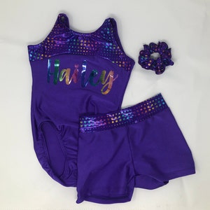 Puede incluir: Un conjunto de maillot, pantalones cortos y coletero morado. El maillot y los pantalones cortos tienen una base morada con un patr&oacute;n de lunares multicolores brillantes en el borde. El maillot est&aacute; personalizado con el nombre "Hailey" en arco&iacute;ris.