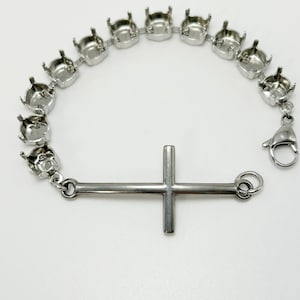 May include: A silver-toned bracelet featuring a series of open-backed settings, connected by links. A horizontal cross is attached to the bracelet with a clasp closure. The bracelet is designed for jewelry making.