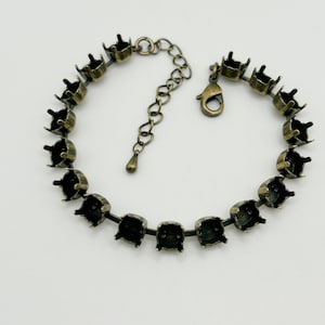 May include: A gold-toned bracelet with a chain and clasp. The bracelet is made of metal settings that are designed to hold gemstones.