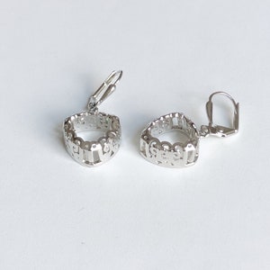 May include: A pair of silver earrings with a delicate, openwork design. The earrings have a circular shape and are attached to a leverback closure.