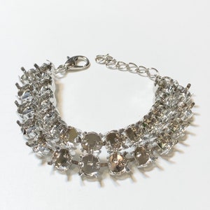 May include: A silver bracelet with a chain and multiple rows of round settings for rhinestones.
