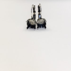 May include: A pair of silver earring settings with a square bezel for a stone. The settings are attached to a hoop.