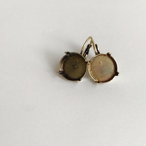 May include: A pair of gold-toned earring settings with round bezels. The bezels are empty and ready to be filled with a stone or other embellishment.