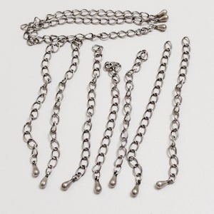 May include: A set of seven silver chains with teardrop-shaped ends. The chains are of varying lengths and are arranged in a fan shape.