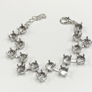 May include: Silver bracelet with a chain and multiple settings for rhinestones. The settings are connected by metal bars.