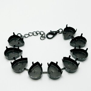 May include: A black metal bracelet with ten teardrop-shaped settings. Each setting has four small prongs. The bracelet includes a chain and a lobster clasp for closure. The settings are connected by small metal bars.