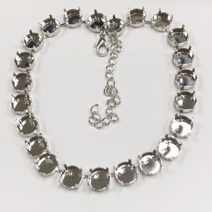 May include: Silver necklace with round settings for rhinestones or other gems. The necklace has a lobster clasp closure.