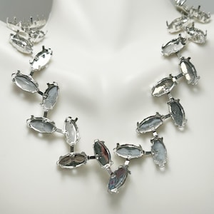 May include: A silver-toned necklace with oval-shaped settings. The necklace is composed of multiple oval settings connected by small bars, creating a unique and modern design. The settings appear to be empty, ready for gemstones or other embellishments.