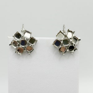 May include: A pair of silver-toned earrings. Each earring features a cluster of small, square-shaped settings, each holding a different colored stone. The stones include shades of silver, black, and brown. The earrings have a lever-back closure.