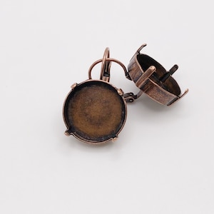 May include: A pair of antique copper-colored leverback earrings. Each earring features a round bezel setting with four prongs and a leverback closure. The earrings are designed to hold a round stone or cabochon.