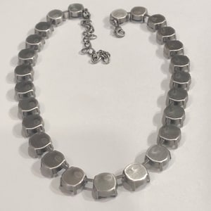 May include: A silver necklace with a chain and round, silver-toned settings for stones. The settings are connected to each other to form the necklace.