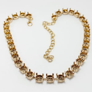 May include: A gold-toned metal necklace chain featuring a series of empty, circular prong settings designed for holding stones. The necklace includes a lobster claw clasp and an adjustable extender chain with a small heart-shaped charm at the end.