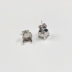 May include: Two silver earring settings for a round stone. The settings have a prong setting and a post with a butterfly back.