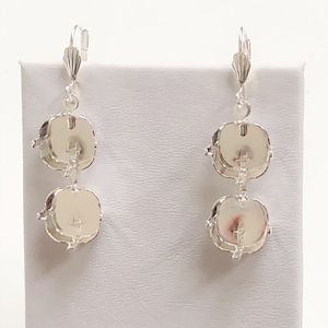 May include: A pair of silver-toned drop earrings. Each earring features two round, light-colored stones with a silver frame. The earrings have a lever-back closure and are displayed on a white surface.
