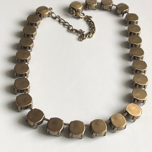 May include: A gold-toned necklace with a chain and round, faceted stones. The necklace is laid out flat on a white surface.