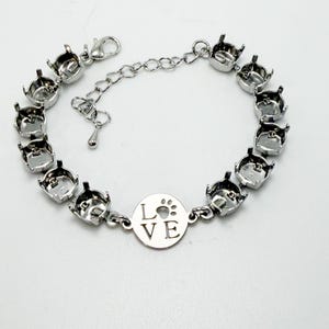 May include: A silver-toned bracelet with a series of bezel settings. A circular charm in the center features the word "LOVE" and a paw print. The bracelet has an adjustable chain closure.