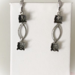May include: A pair of silver-toned earrings. Each earring features a lever back closure, a square-shaped setting, an oval link, and another square setting. The earrings are displayed against a white background.