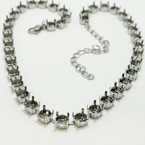 May include: A silver-colored necklace with multiple settings for stones. The necklace has a chain with a lobster clasp and an extender chain. The settings are evenly spaced and designed to hold round gemstones. The necklace is on a white background.