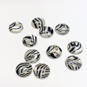 May include: A collection of 11 round, white cabochons with black zebra stripe patterns.