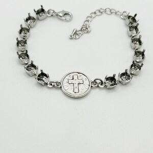 May include: Silver-toned bracelet with a religious theme. The bracelet features a series of empty settings for stones, connected by small links. A central medallion displays a cross. The bracelet has an adjustable chain and a lobster clasp.