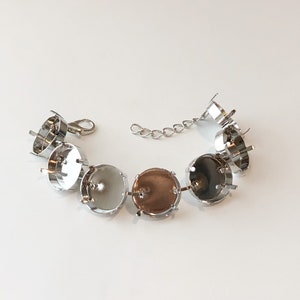 May include: A silver-toned bracelet with seven round settings, each designed to hold a stone or cabochon. The bracelet has a lobster clasp closure and an extender chain for adjustable sizing. The settings are empty, ready for customization.