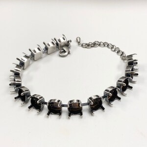May include: A silver bracelet with a chain clasp and multiple settings for gemstones. The settings are empty and ready to be filled with stones.