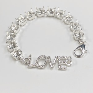 May include: A silver bracelet with a series of square settings, connected by small links. The word "LOVE" is spelled out in silver letters, each encrusted with small, clear crystals. A silver clasp secures the bracelet.