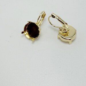 May include: Two gold-colored leverback earring findings. One finding has a round, open setting, and the other has a solid, rounded back. The findings are on a white surface.