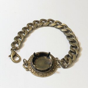 May include: A gold-toned bracelet with a large round bezel setting. The bracelet is made of a thick curb chain.
