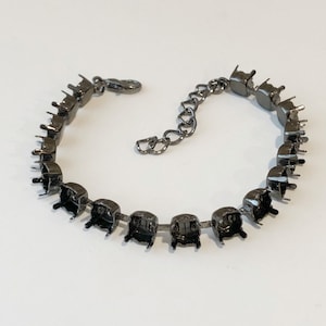 May include: A gunmetal-toned bracelet base featuring a series of empty, pronged settings designed for holding stones. The bracelet includes a lobster claw clasp and an adjustable extender chain with larger links for a customizable fit.