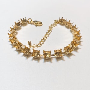 May include: Gold-toned bracelet with square settings designed to hold gemstones. The bracelet features a delicate chain for adjustable sizing and a secure clasp. The settings are evenly spaced along the bracelet's length, creating a symmetrical design. The bracelet is displayed on a white background.
