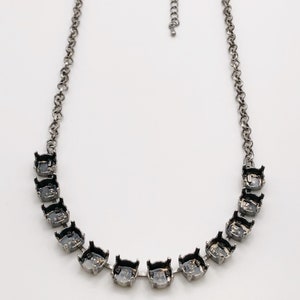 May include: A silver-toned necklace featuring a series of clear, faceted stones set in black metal prongs. The chain is a simple link design with an adjustable clasp. The necklace is displayed against a white background.