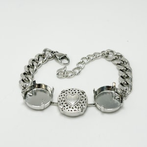 May include: Silver-toned bracelet featuring a chain design with three circular settings. The central setting has a heart design. The bracelet has a lobster clasp closure. The bracelet is made of metal.
