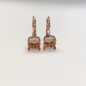 May include: A pair of rose gold earring settings with a square shape. The settings are open on the back and have a lever back closure.