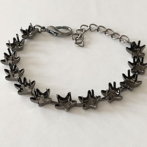 May include: A black metal bracelet with a chain and star-shaped charms. The bracelet is made of metal and has a dark finish.